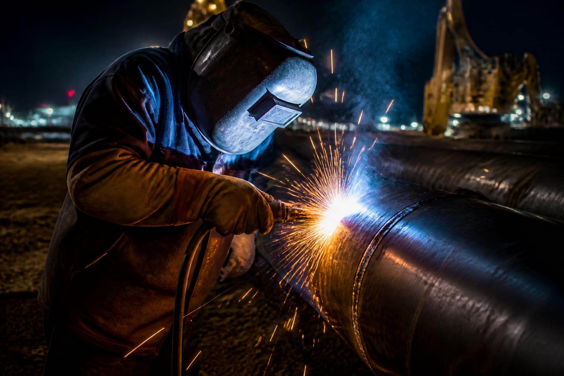 Welder joining large pipeline sections with sparks flying